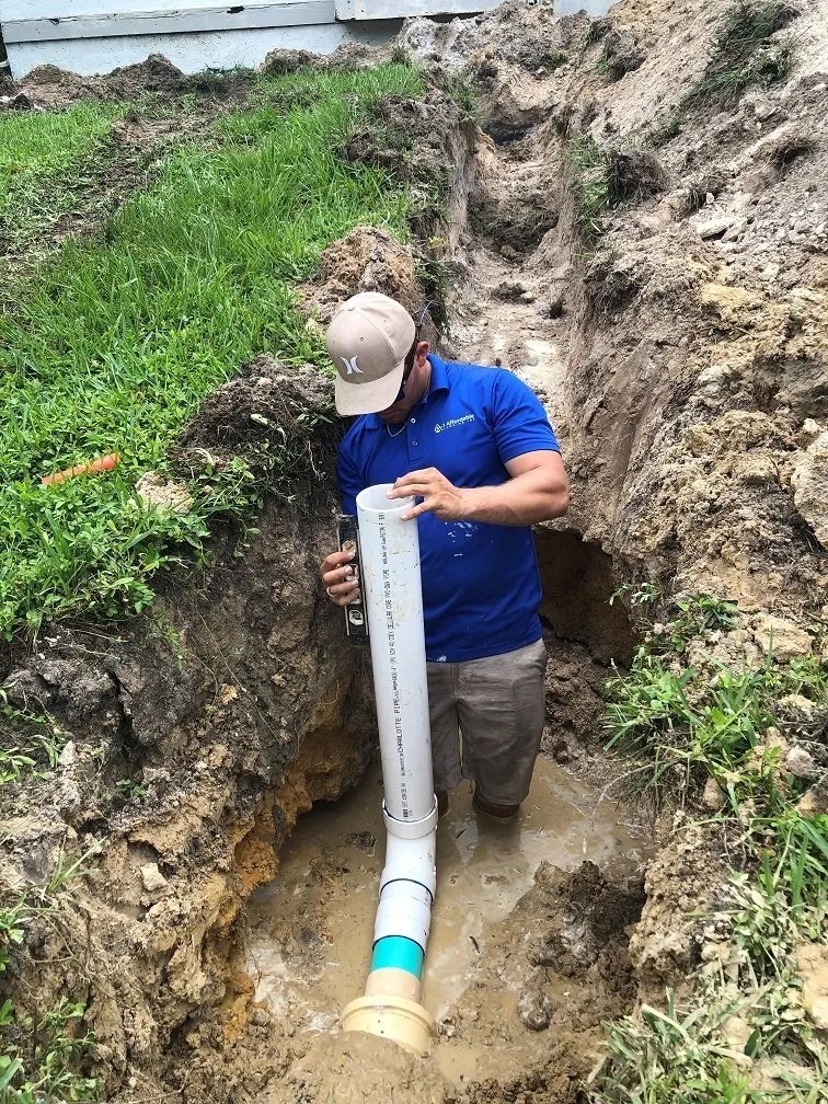 Plumber standing in a trench dug by an excavator installing a clean-out on a new sewer line installed due to a crack in the old sewer line